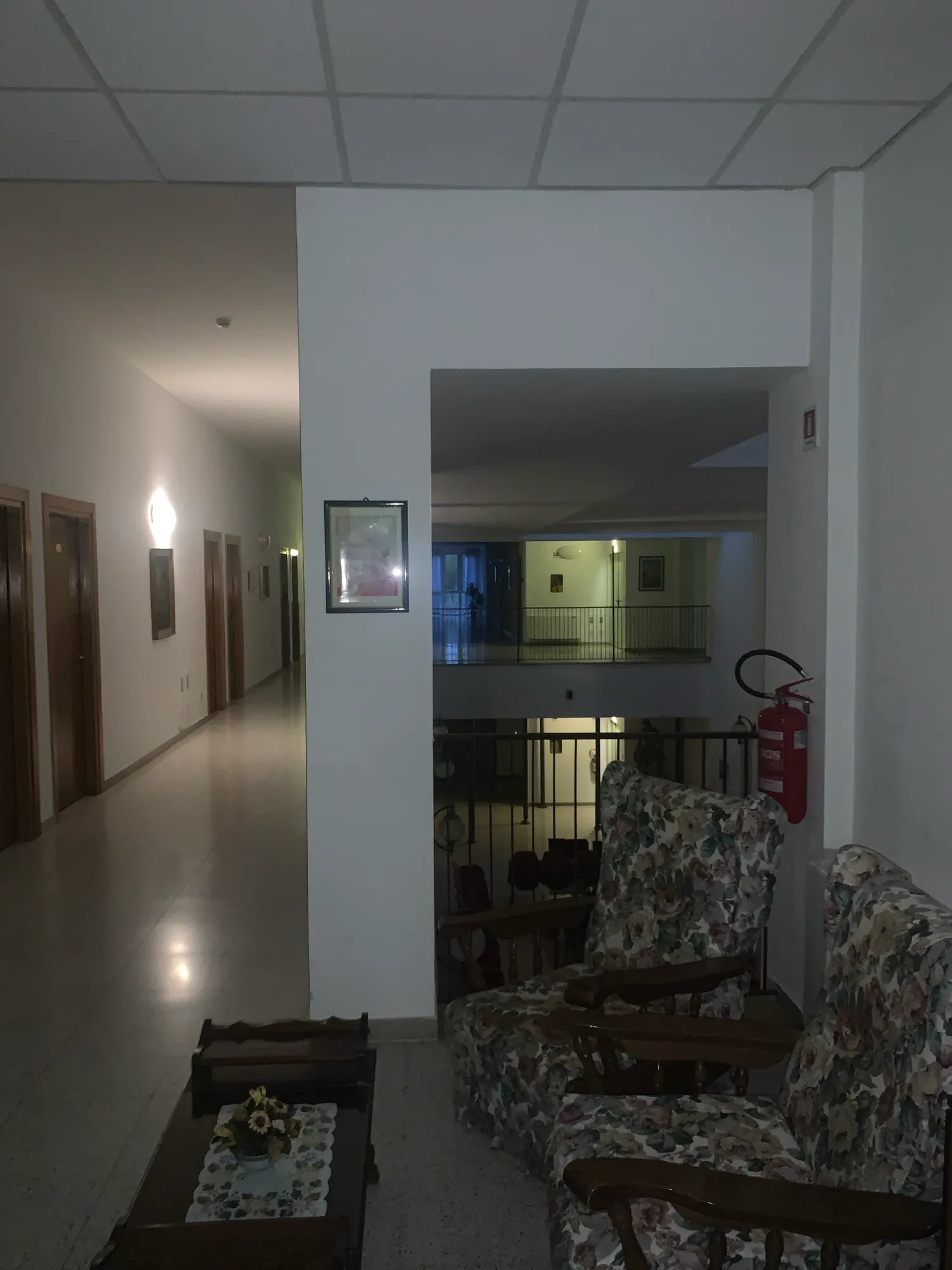 Dämmriger Flur mit Sesseln und einem Feuerlöscher, Durchblick in den offenen Treppenraum