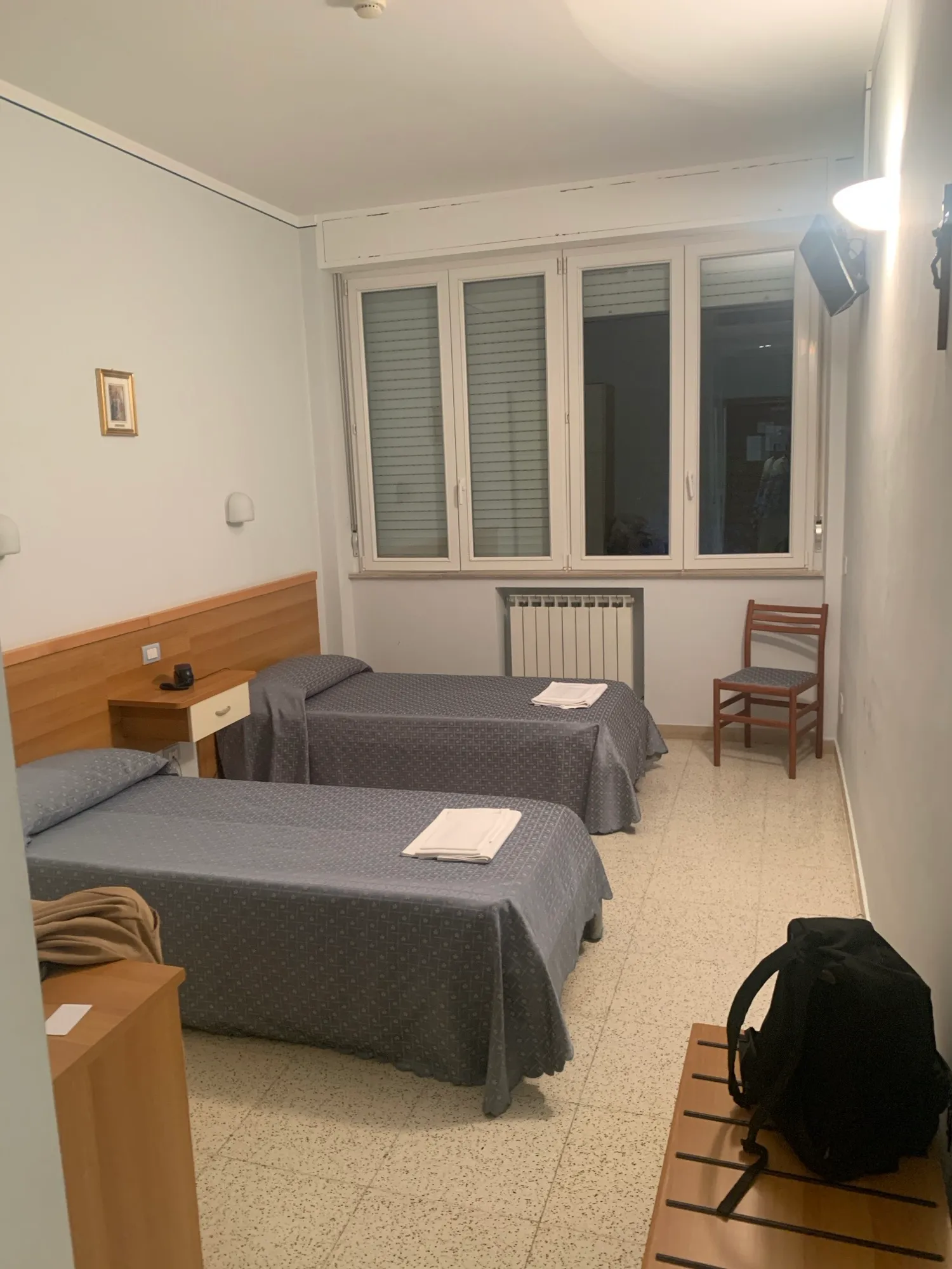 Doppelzimmer mit zwei Betten, Fenster mit Jalousien, Heizkörper und Holzstuhl