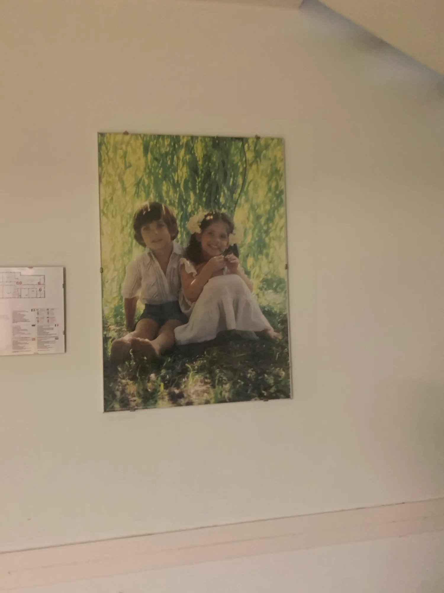 Großformatiges Foto zweier Kinder im Gras, an der Wand neben einem Aushang